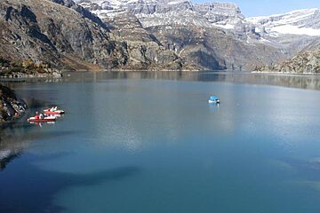 Three pedal boats are floating on a lake with mountains in the background