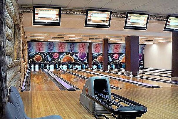 A bowling alley with a lot of bowling pins and televisions hanging from the ceiling