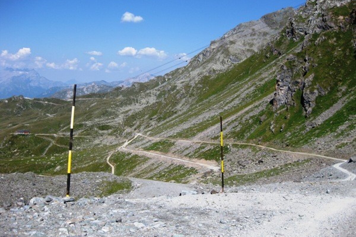 A dirt road in the mountains with a yellow pole in the foreground