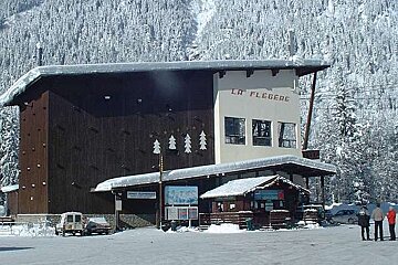 A large building is covered in snow in the middle of a snowy forest
