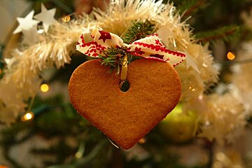 A heart shaped gingerbread ornament hangs from a christmas tree