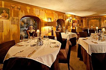 an image of a room with 2 round tables with white cloths on and wine glasses
