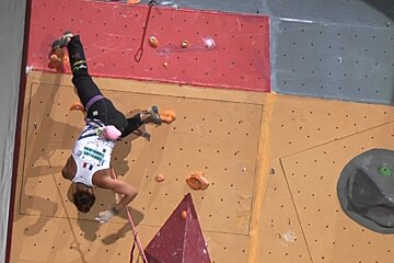 A person is doing a handstand on a climbing wall and they are wearing a shirt that says ' barcelona '