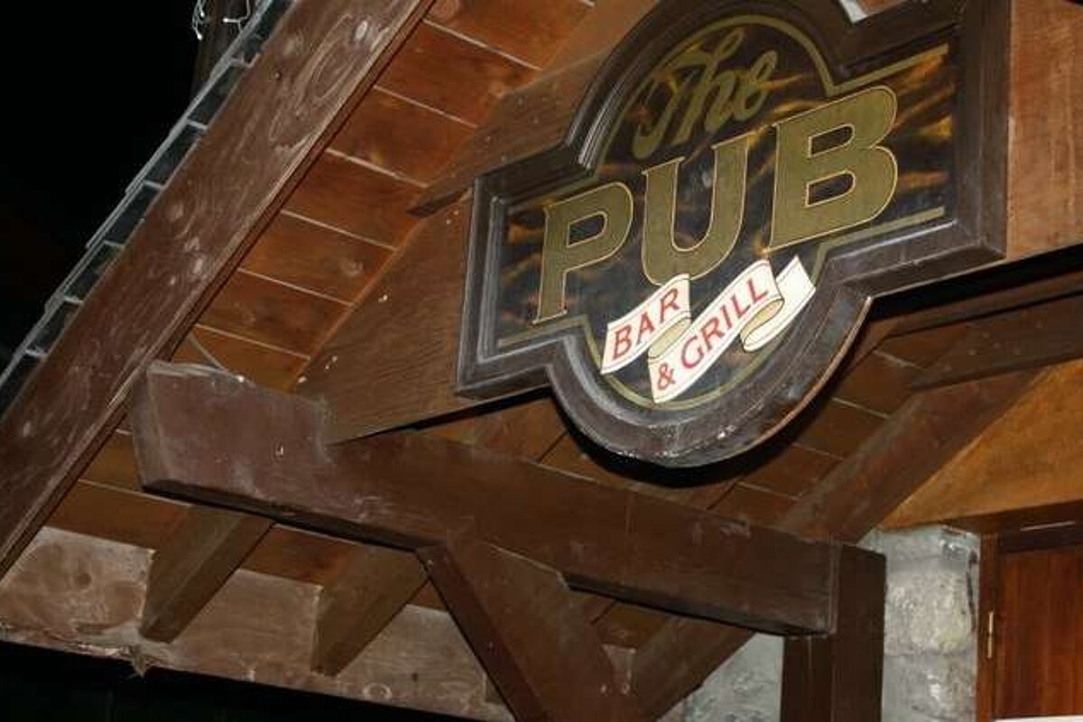 A sign for the pub bar and grill is hanging from the roof of a building