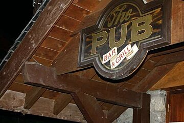 A sign for the pub bar and grill is hanging from the roof of a building