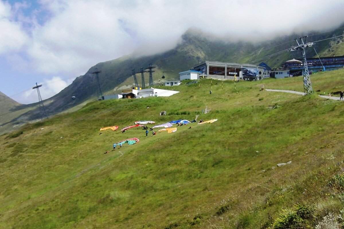 A group of people are paragliding down a grassy hill