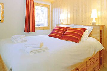 an image of a room with a double bed with white sheets and red cushions and curtains