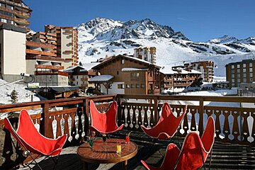 A balcony with red chairs and a table with a mountain in the background