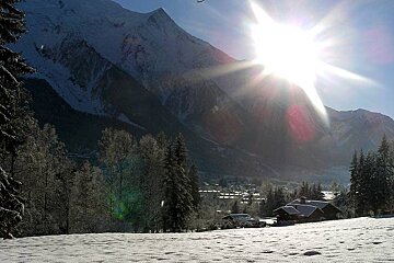 The sun shines brightly over a snowy mountain range