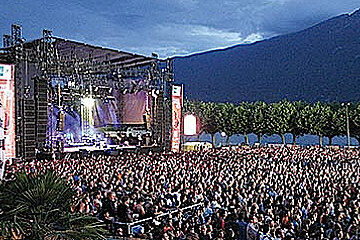A large crowd of people are watching a concert in front of a mountain
