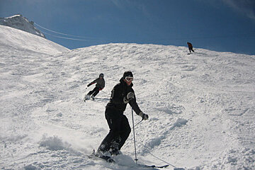 Two people skiing down a snow covered slope on a sunny day
