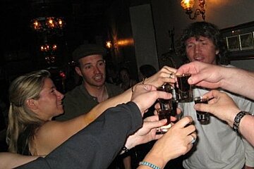 A group of people are toasting with shot glasses in a dark room