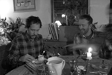 A man in a plaid shirt sits at a table with a pitcher of water and a candle