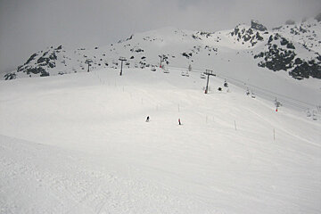 A person skiing down a snowy slope with ski lifts in the background