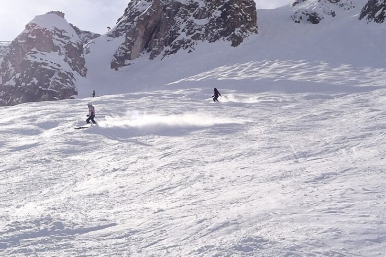 People skiing down a snow covered slope with mountains in the background