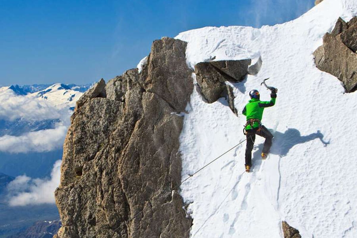 A man in a green jacket is climbing a snowy mountain