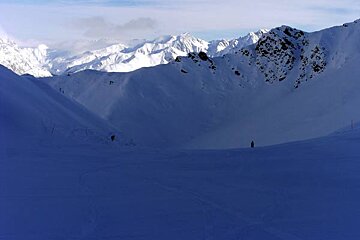 People skiing down a snowy slope with mountains in the background