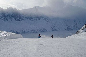 Two people are skiing down a snow covered slope in the mountains