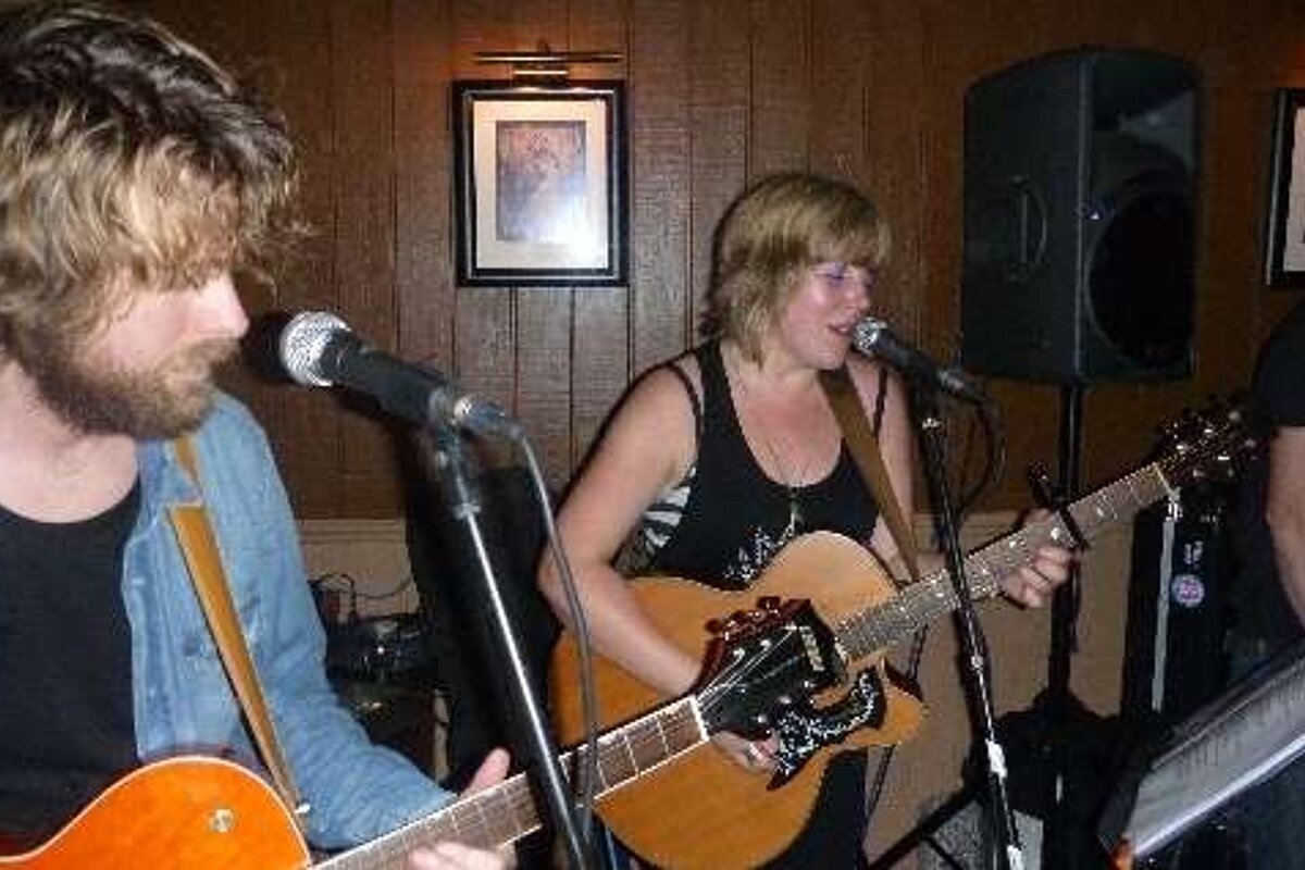 A man and a woman are playing guitars and singing into microphones