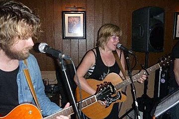 A man and a woman are playing guitars and singing into microphones