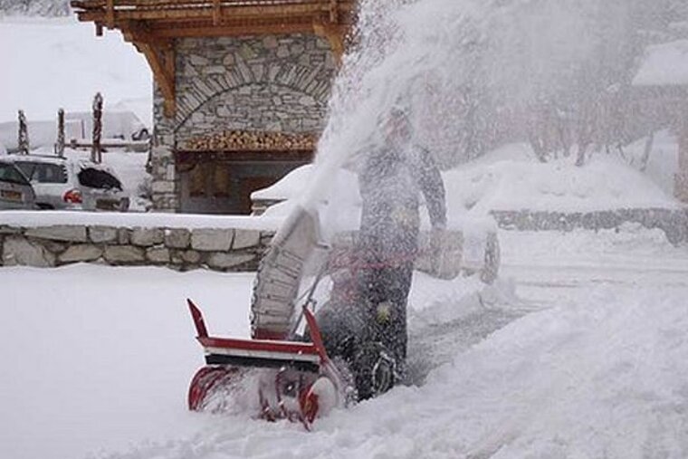 A man is using a snow blower to remove snow from a driveway