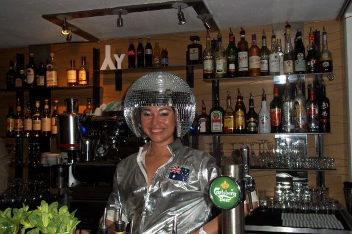 A bartender wearing a disco ball hat and a carlsberg beer tap