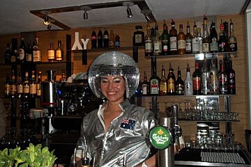 A bartender wearing a disco ball hat and a carlsberg beer tap