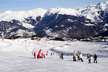 Skiers on a snowy slope with mountains in the background