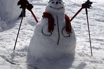 A snowman wearing skis and a scarf has the letter c on his face