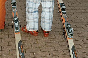 A person is standing on a brick sidewalk with skis on their feet