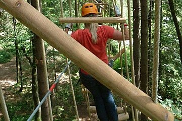 A woman wearing a helmet is standing on a ropes course in the woods