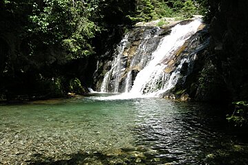 A waterfall is surrounded by trees and a body of water