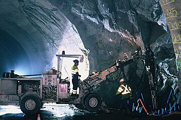 Two men are working in a tunnel with the number 210 on the wall
