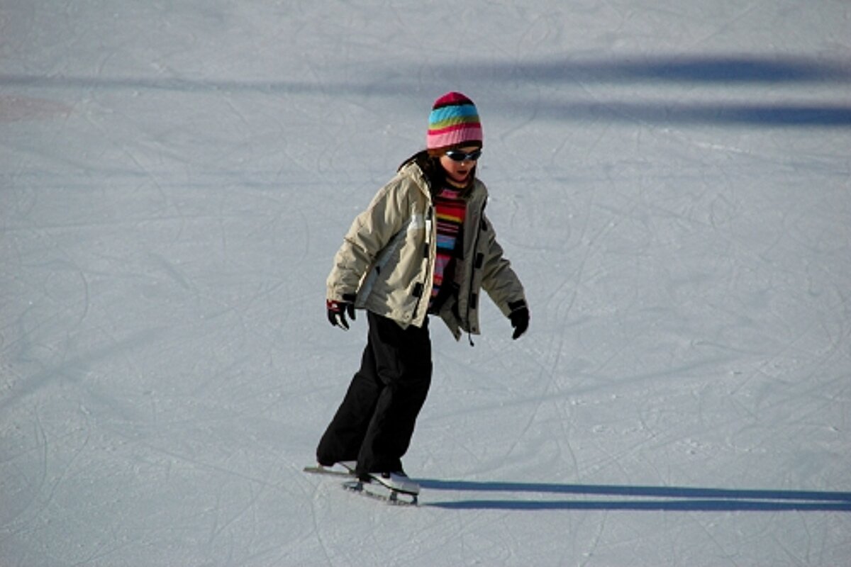 A person wearing a hat and sunglasses is ice skating