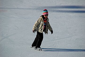 A person wearing a hat and sunglasses is ice skating