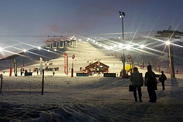 People walking down a snowy ski slope at night