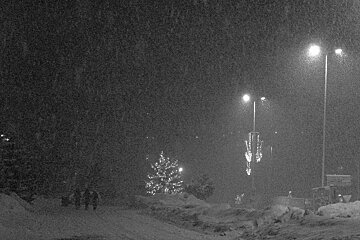 A black and white photo of a snowy street at night
