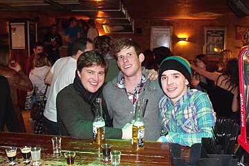 Three men are sitting at a bar holding bottles of corona beer