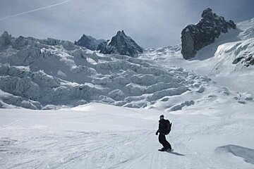 A snowboarder is riding down a snow covered slope with mountains in the background