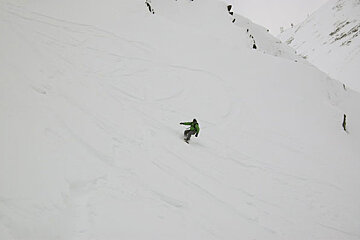 A person in a green jacket is skiing down a snow covered slope