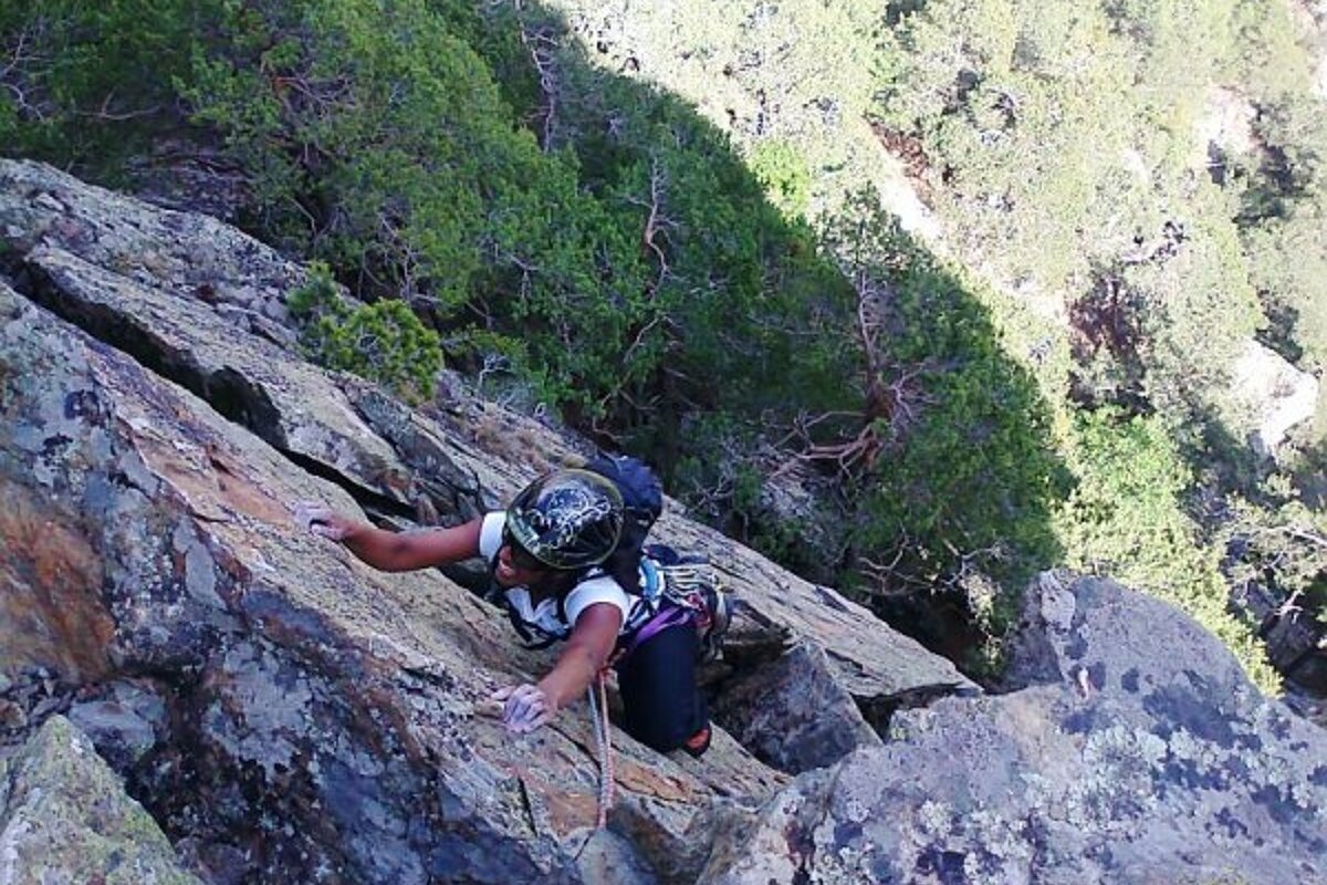 A person wearing a helmet is climbing up a rocky cliff
