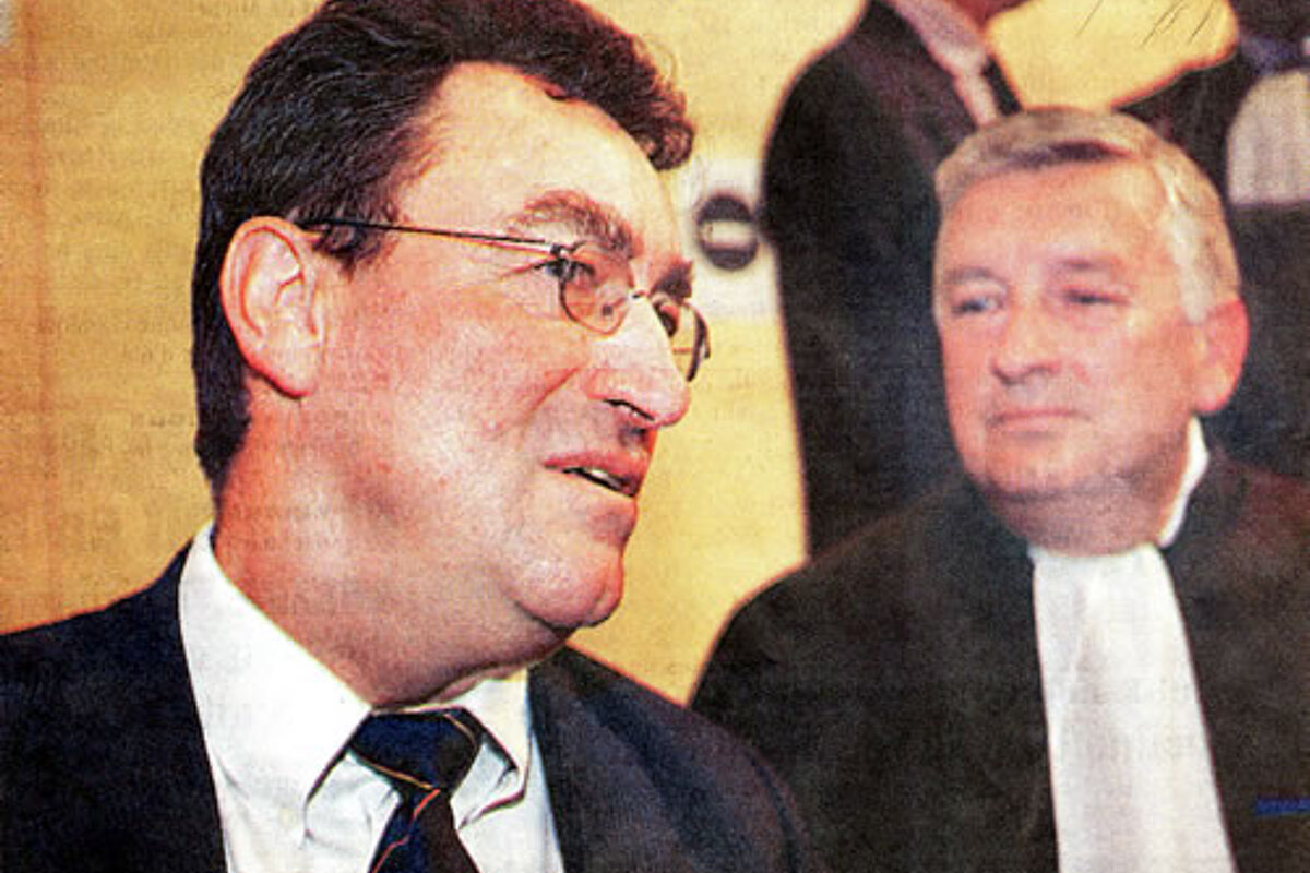 A man in a suit and tie stands next to another man in a suit and tie