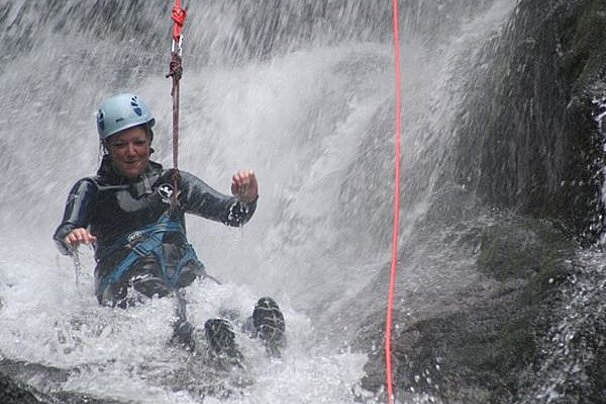 A woman wearing a helmet is sitting in a waterfall