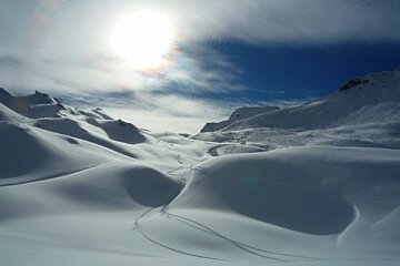 A snowy mountain with the sun shining through the clouds
