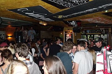 A crowd of people are gathered in a bar with a coca cola sign on the ceiling