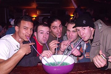 A group of men drinking through straws with one wearing a ny hat