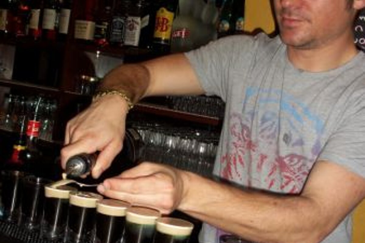 A man is pouring a drink into shot glasses at a bar
