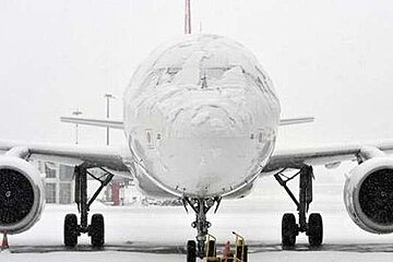 A large passenger jet covered in snow is parked on a runway