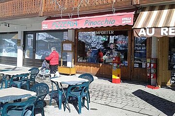 A woman pushes a stroller in front of a pizzeria