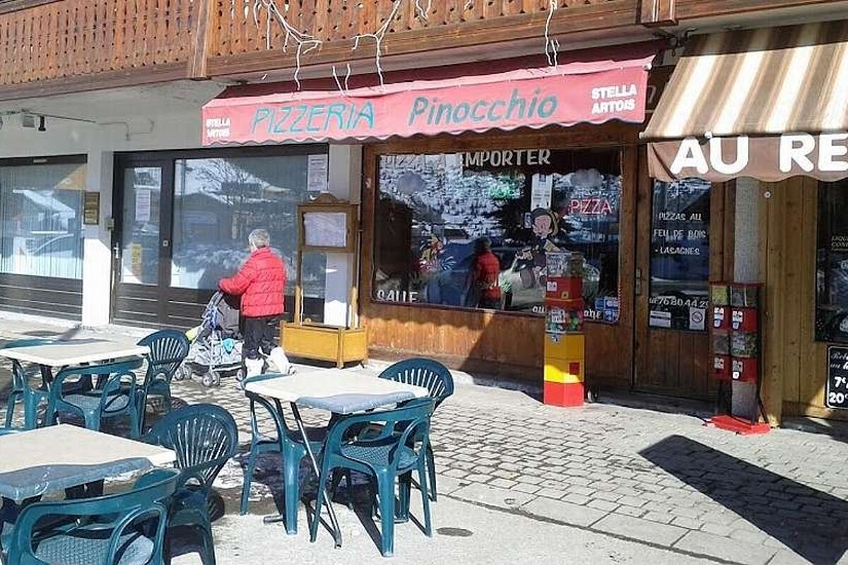 A woman pushes a stroller in front of a pizzeria